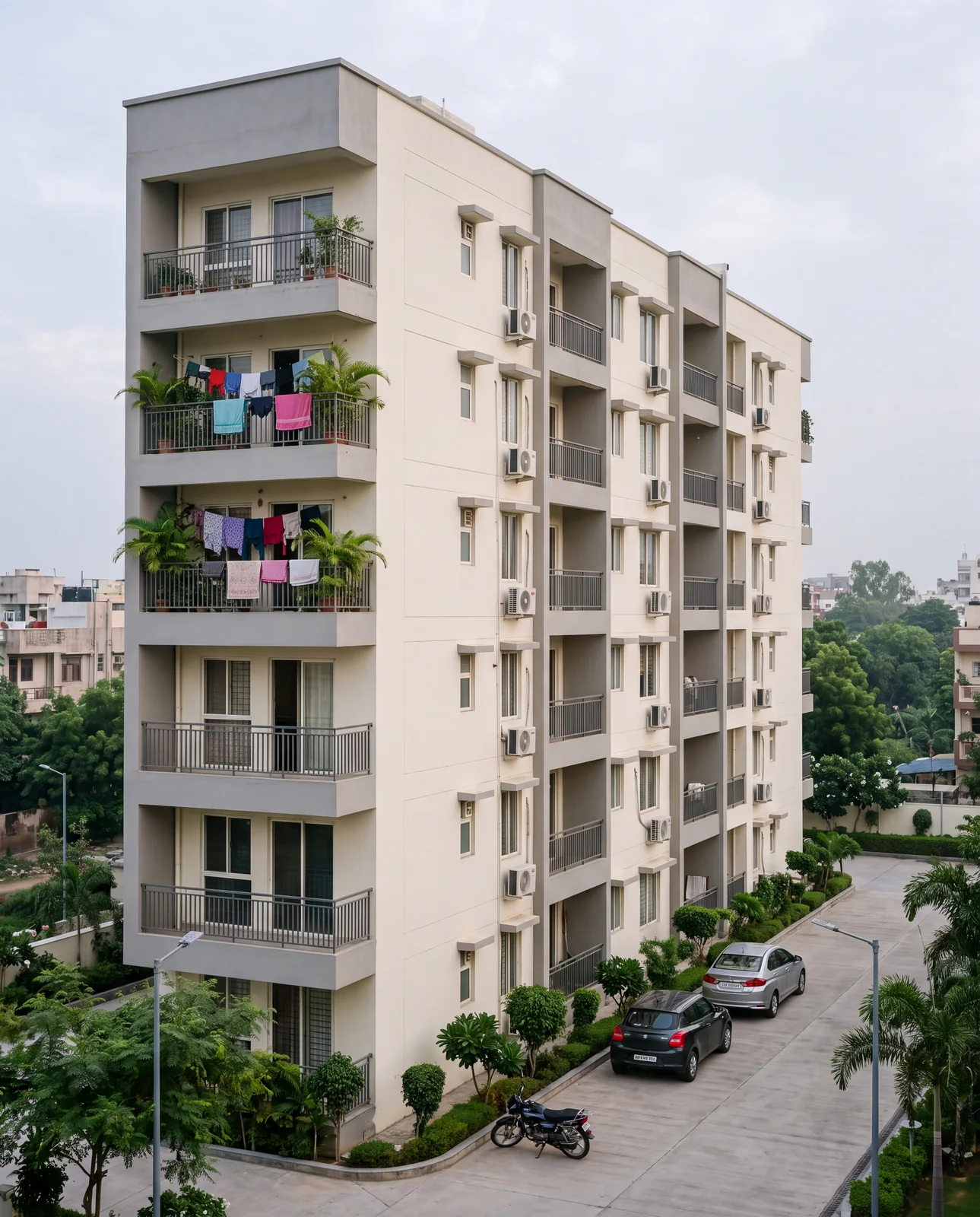 A six-storey cream apartment block with balconies, washing on the railings and two cars parked below
