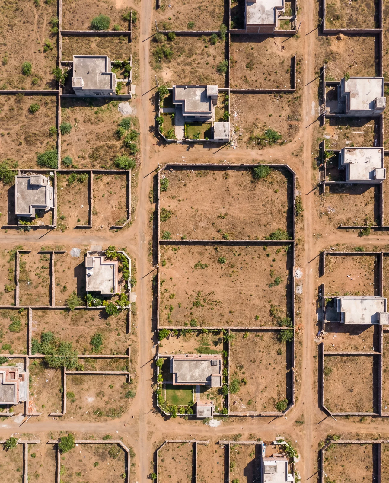 Seen straight down from the air, a grid of walled plots and dirt roads with a few flat-roofed houses built on some of them and the rest bare earth.